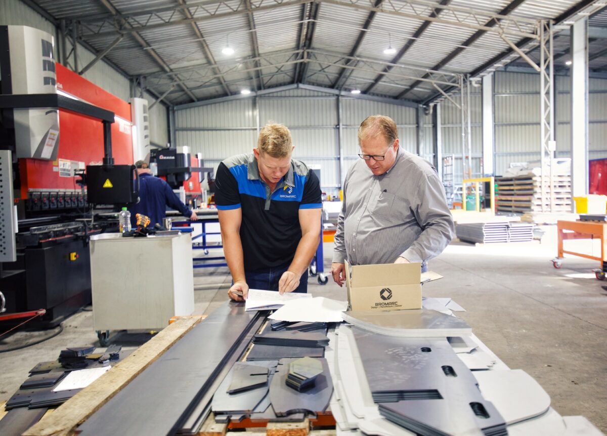 Joel Muller and Jon Muller discussing design of latest project while at laser table. The table is spread with CNC laser cut parts, they are in their large Australian Manufacturing Facility.